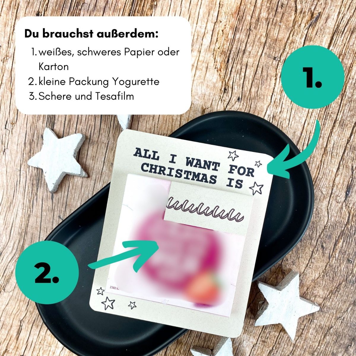 Karte mit dem Text „All I want for Christmas is You“ liegt auf schwarzer Schale, daneben weiße Sterne. Auf dem Bild steht: „Du brauchst außerdem: 1. weißes Papier oder Karton, 2. kleine Packung Yogurette, 3. Schere und Tesafilm“. Perfekte Anleitung für ein kleines Geschenk zu Weihnachten.