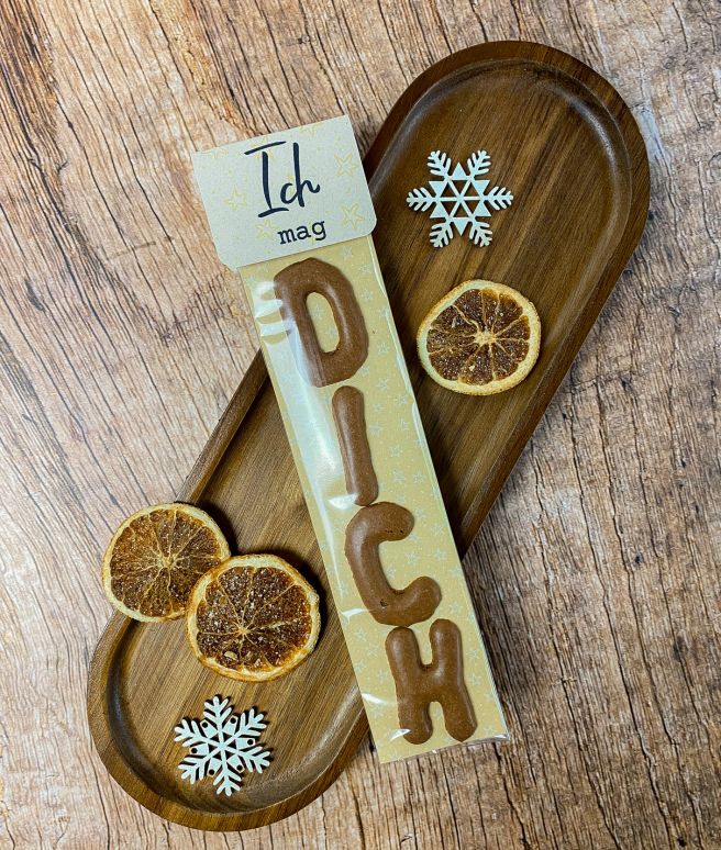 Süßes Weihnachtsgeschenk mit Schokolade in Buchstabenform „DICH“, Karte mit Aufschrift „Ich mag“. Dekoriert mit Schneeflocken und getrockneten Orangenscheiben auf Holztablett. Witzige kleine Geschenkidee zu Weihnachten.