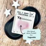 Karte mit Aufschrift „All I want for Christmas is You“ und Platz für eine Yogurette-Schokolade. Liegt auf schwarzer Schale mit weißen Holzsternen. Liebevolle Druckvorlage für ein kleines Weihnachtsgeschenk zum Selbermachen.