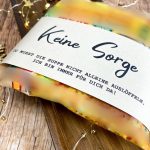 Nahaufnahme der fertig gebastelten Tütensuppe mit beige farbener Banderole. Aufdruck: „Keine Sorge – du musst die Suppe nicht alleine auslöffeln“. Liebevoll fotografiert auf Holzuntergrund – kreative Geschenkidee zum Schmunzeln.