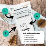 Schritt-für-Schritt-Anleitung mit nummerierten Pfeilen erklärt, wie man die Druckvorlage „Wellness statt Weihnachtsstress“ bastelt. Zeigt Materialien wie Gesichtsmaske, Schere und Tesafilm auf Holzuntergrund mit Weihnachtsdeko. Perfekte kleine Aufmerksamkeit im Advent.