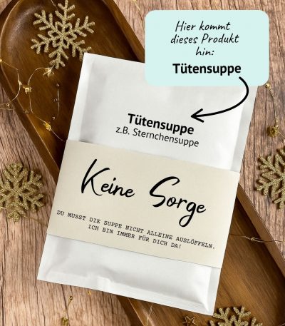 DIY Druckvorlage für eine Tütensuppe mit der Aufschrift „Keine Sorge – du musst die Suppe nicht alleine auslöffeln“. Die Suppe steckt in einer liebevoll gestalteten Banderole, umgeben von Holzdeko und goldenen Schneeflocken. Humorvolle Geschenkidee zum Ausdrucken.