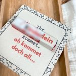 Nahaufnahme einer fertig gebastelten Karte mit integrierter Kinderschokolade. Aufdruck „Ihr Kinderlein kommet, oh kommet doch all…“ mit verspieltem Sternenrand. Liegt auf hellem Holzhintergrund – charmante DIY-Idee für Wichtelgeschenke oder Adventskalender.