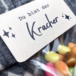 Detailaufnahme der MAOAM Kracher Geschenkidee mit Etikett „Du bist der Kracher“ auf Kraftpapier und bunter Bonbonmischung.