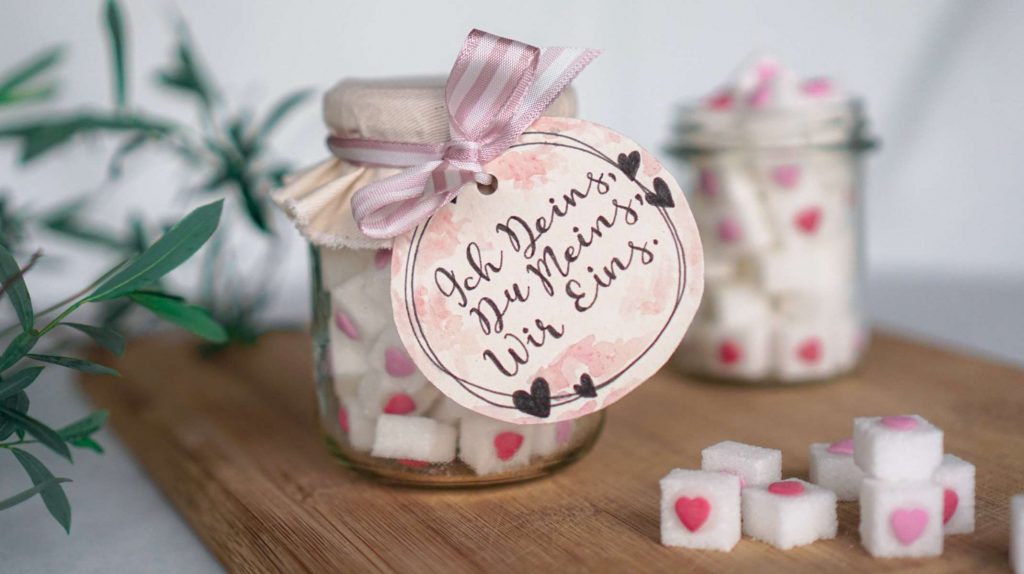 Nahaufnahme von Zuckerwürfeln mit kleinen Herzchen und Hochzeitsanhänger mit der Aufschrift „Ich Deins. Du Meins. Wir Eins.“.