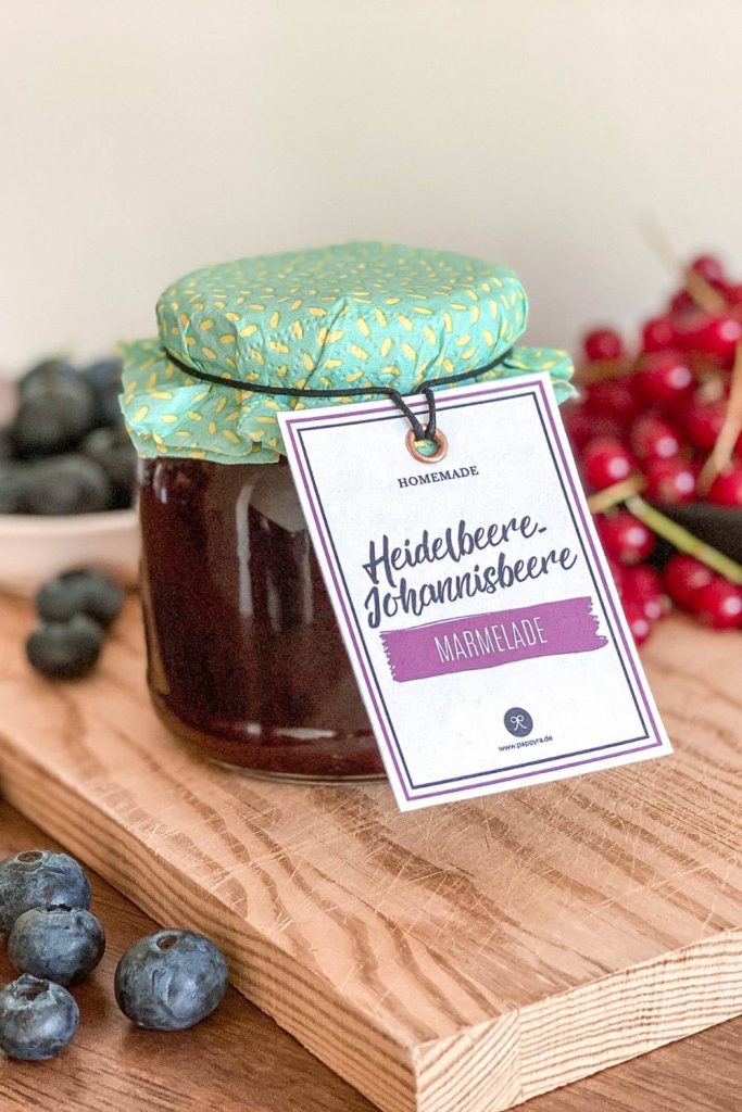 Selbstgemachte Marmelade mit Johannisbeere und Heidelbeere in einem Altglas, dekoriert mit Geschenkband und Etikett zum Ausdrucken.