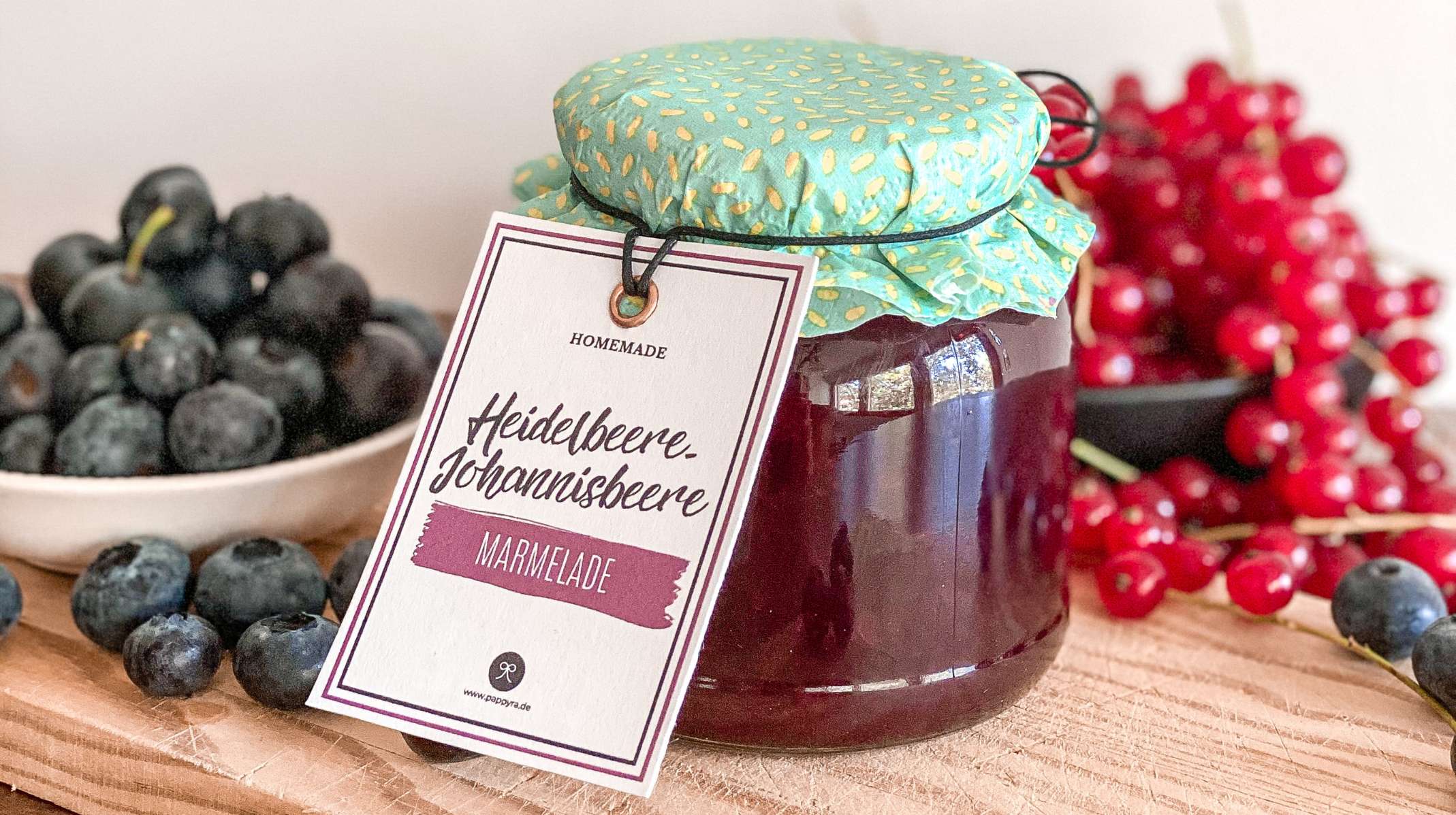 Nahaufnahme eines Etiketts für Marmelade mit Johannisbeere und Heidelbeere, angebunden an ein Glas als Geschenk aus der Küche.